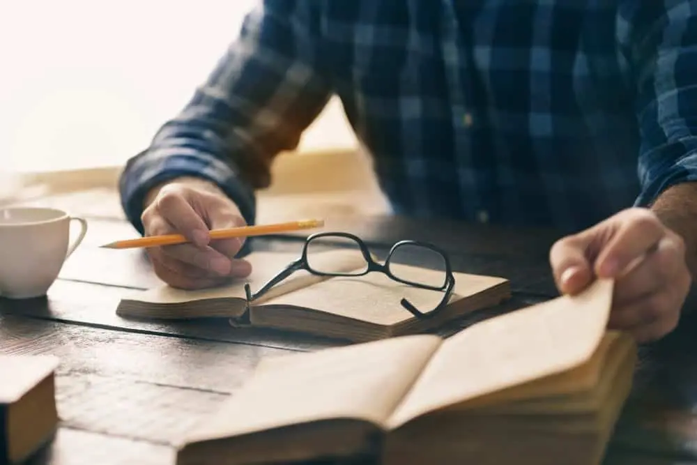 A college student studying at a desk with a textbook, pencil, and glasses