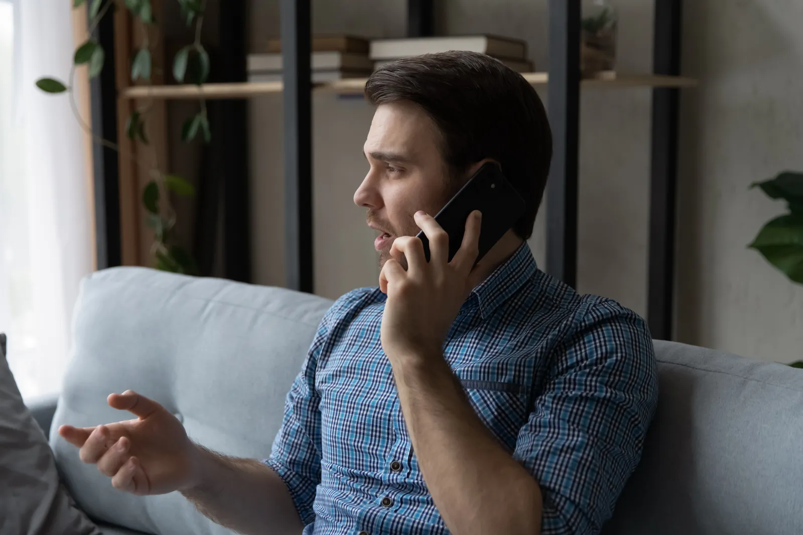 A man seated on a sofa at home talks on his phone.