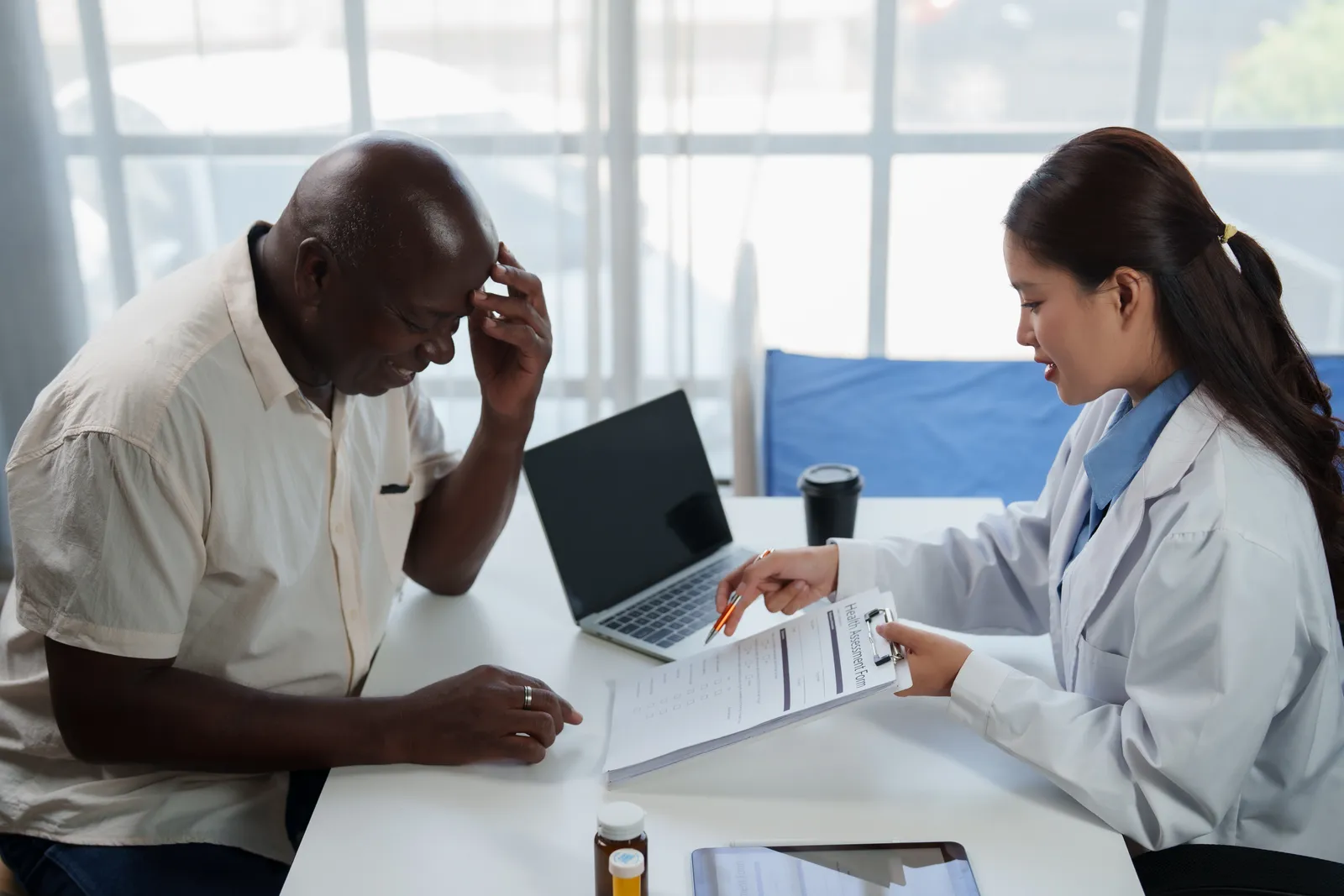 A doctor reviews a health assessment form with an older man at a clinic desk.