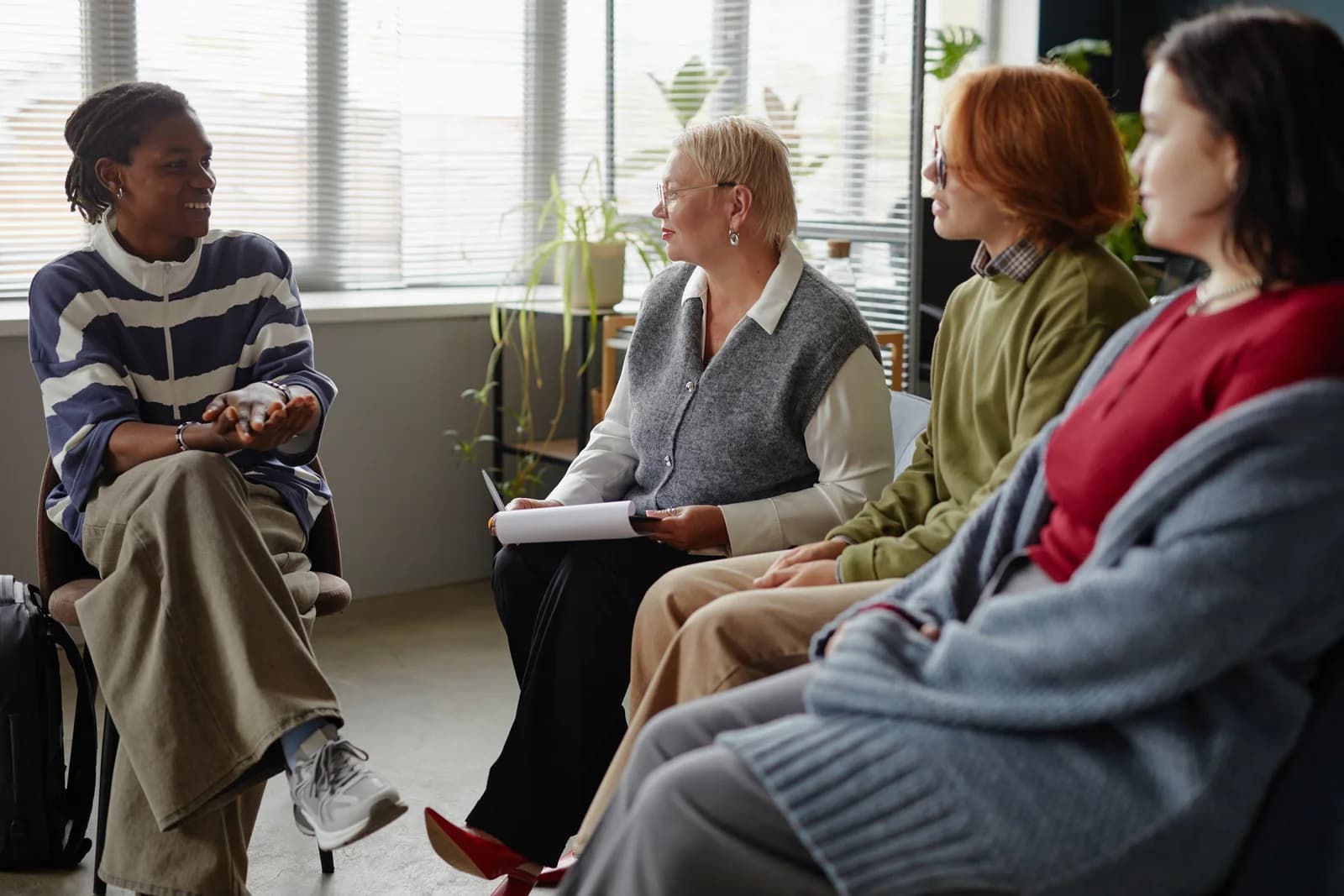Four adults sit in a circle during a group discussion, with one participant holding a notepad.